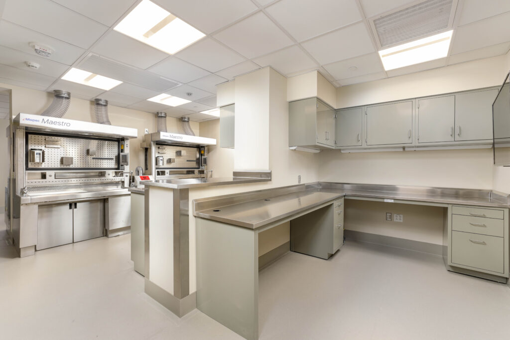 Laboratory room with two stainless steel Mopec Maestro workstations and stainless steel countertops with grey cabinets.