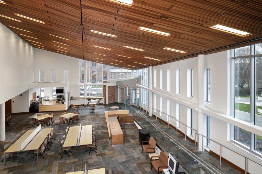 High-angle view of a library interior featuring a slatted wood ceiling, rows of study desks, and tall windows.