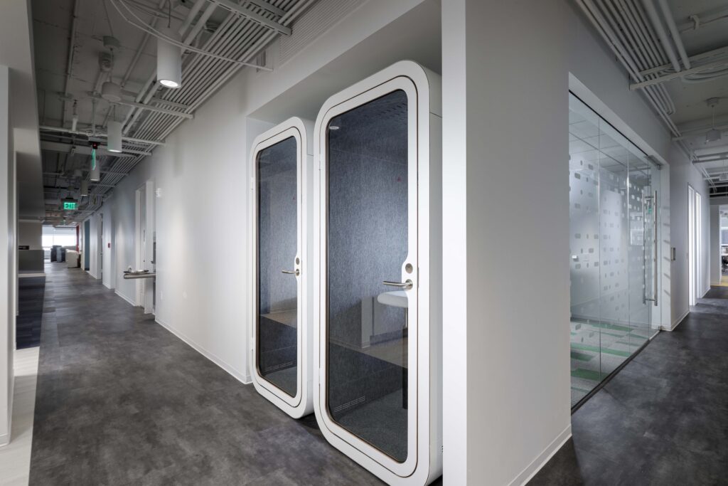 Two white, glass-fronted soundproof office pods installed in a hallway.