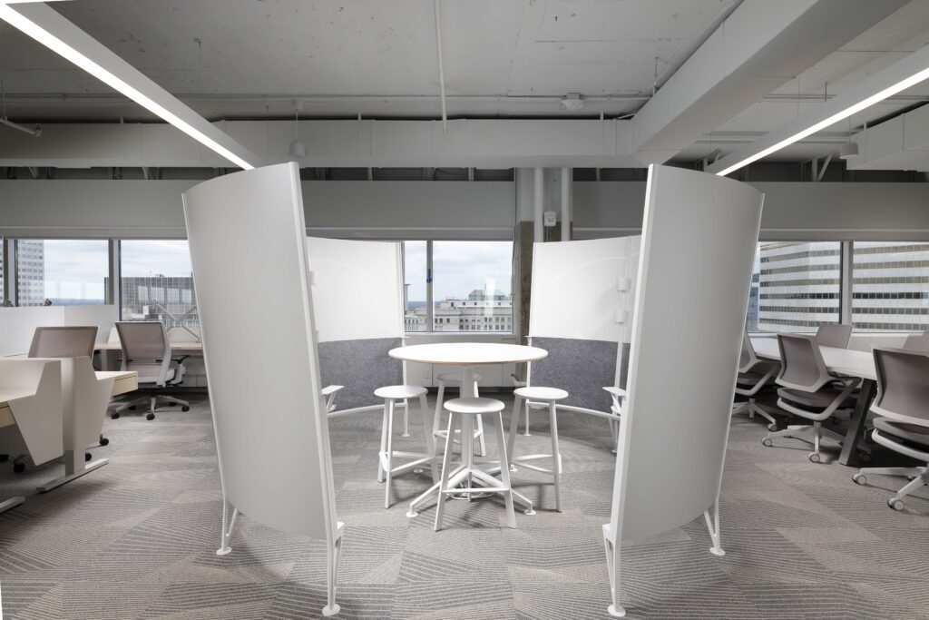 A small round table with four stools, enclosed by white curved privacy screens in a modern office space.