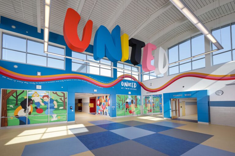 School lobby with a large “UNITED” sign hanging from the ceiling and colorful murals on the walls.