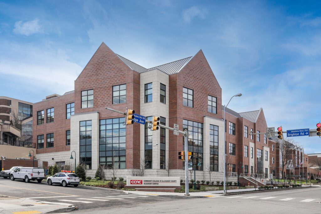 Exterior of a multi-story red brick and stone Community College of Allegheny County building on a corner lot with traffic signals and signage.