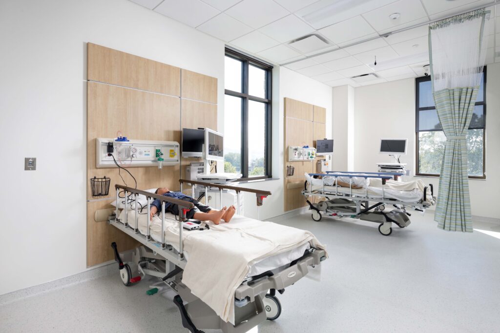 A medical simulation room with two hospital beds, each occupied by a medical training mannequin.