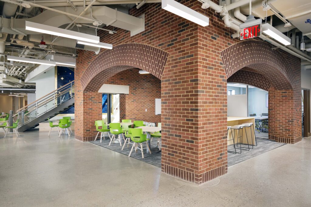 An office lobby with brick archways, lime green chairs, and a kitchen island with stools.