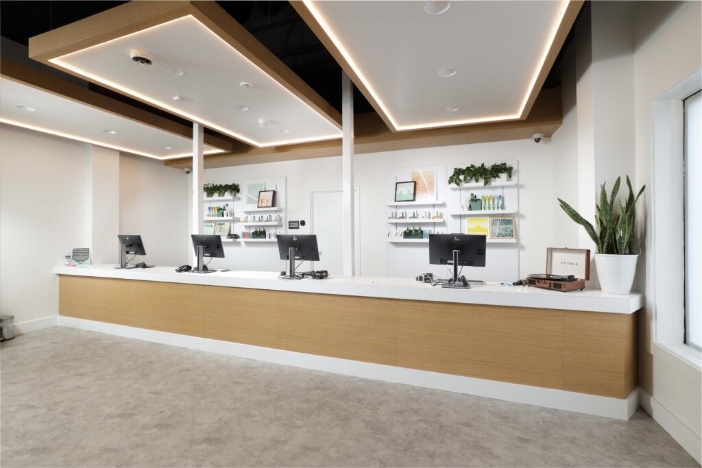 Long reception desk with four computer workstations, wood-paneled front, and shelving units displaying products on the wall behind it.