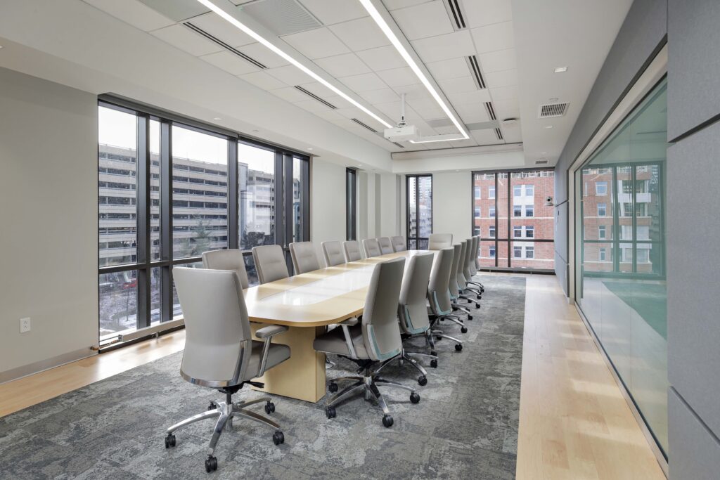 A long conference table surrounded by grey rolling chairs in a modern office with floor-to-ceiling windows.