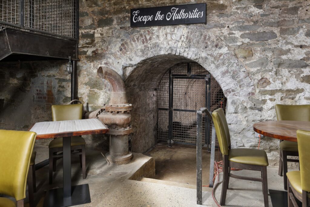 A dining area featuring a stone archway with a metal gate and a sign that reads “Escape the Authorities.”