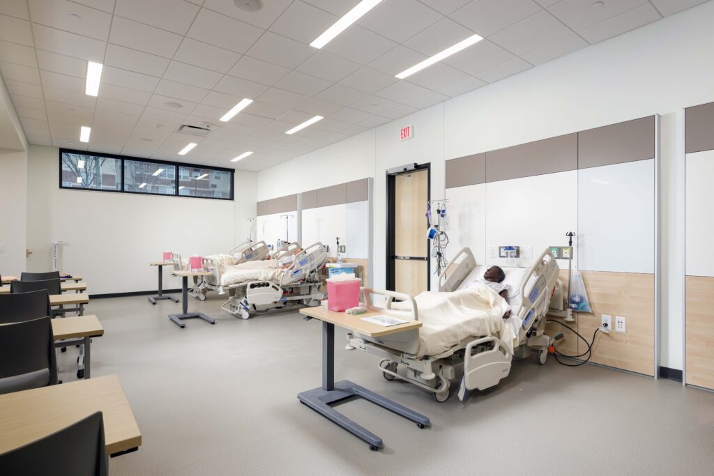 A hospital ward with two patient beds, each equipped with medical monitors and an over-bed table.