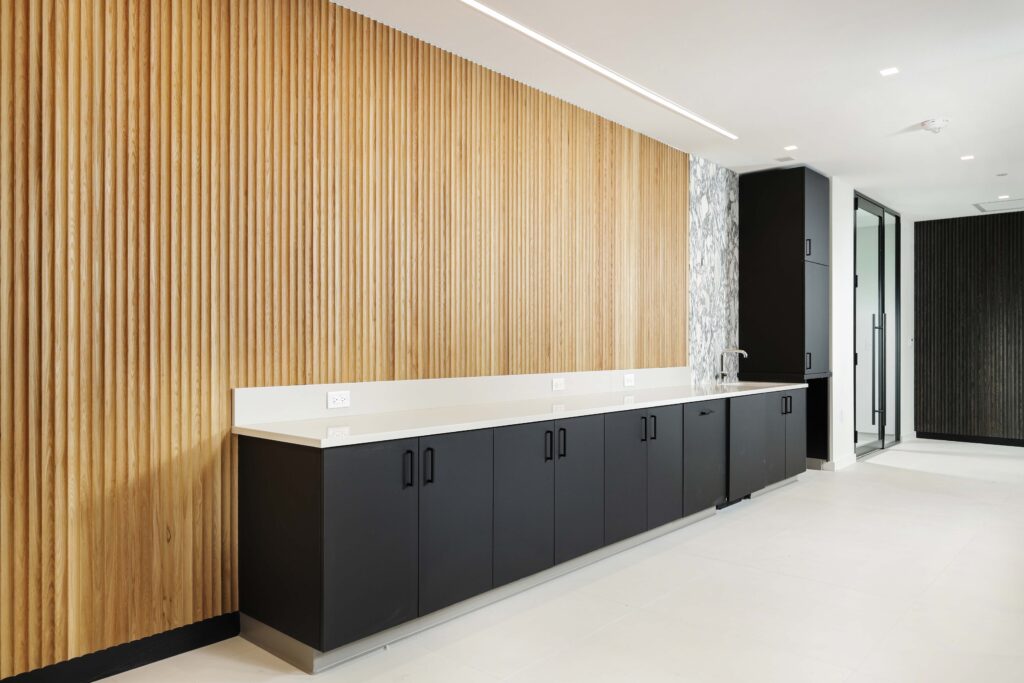 A kitchenette featuring black lower cabinets, a white countertop, and a wall covered in vertical wooden slats.