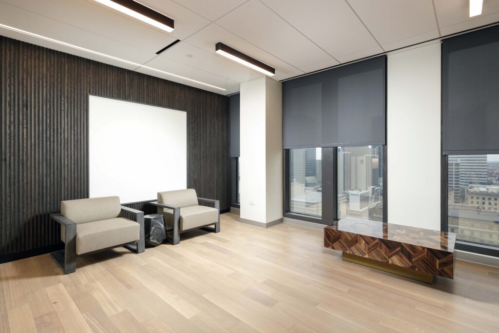 A waiting area with two upholstered armchairs, a small side table, and a low geometric coffee table in a room with light wood floors and dark wood paneling.