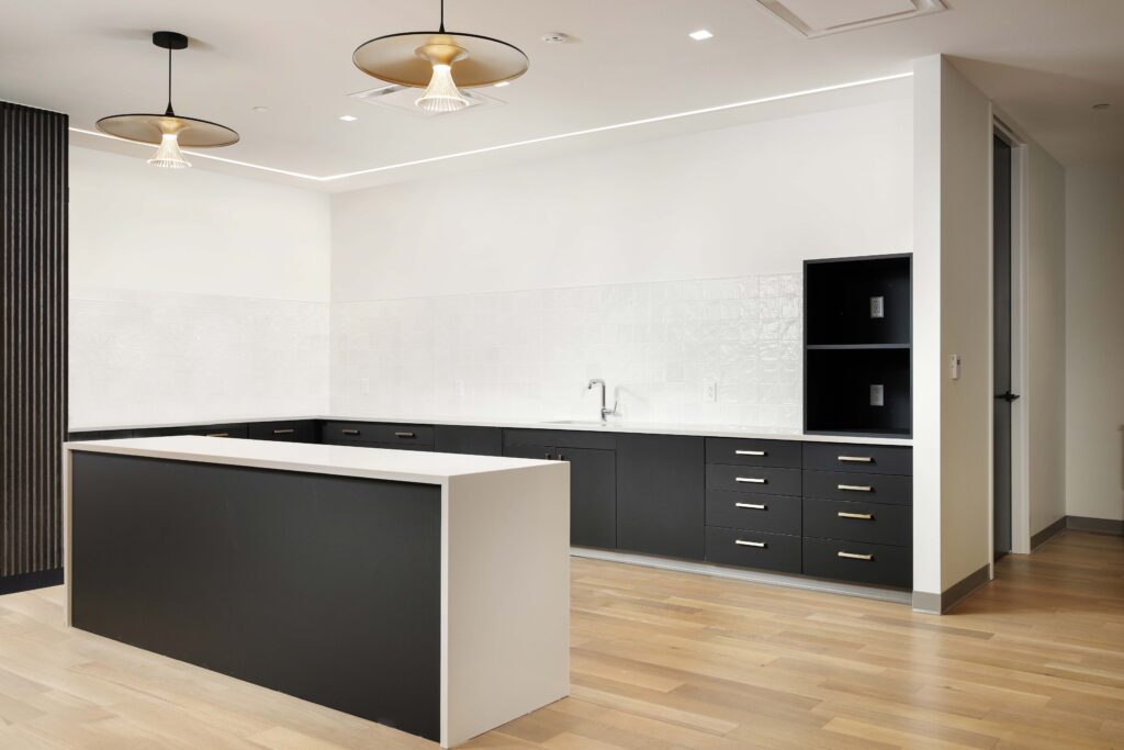 Modern kitchen with an L-shaped island, matte black cabinets, white countertops, a white tiled backsplash, and two pendant lights.