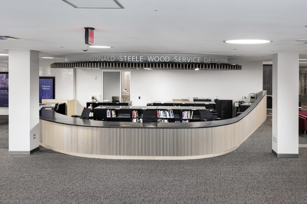 A curved service desk labeled “Donald Steele Wood Service Desk” in a library setting.