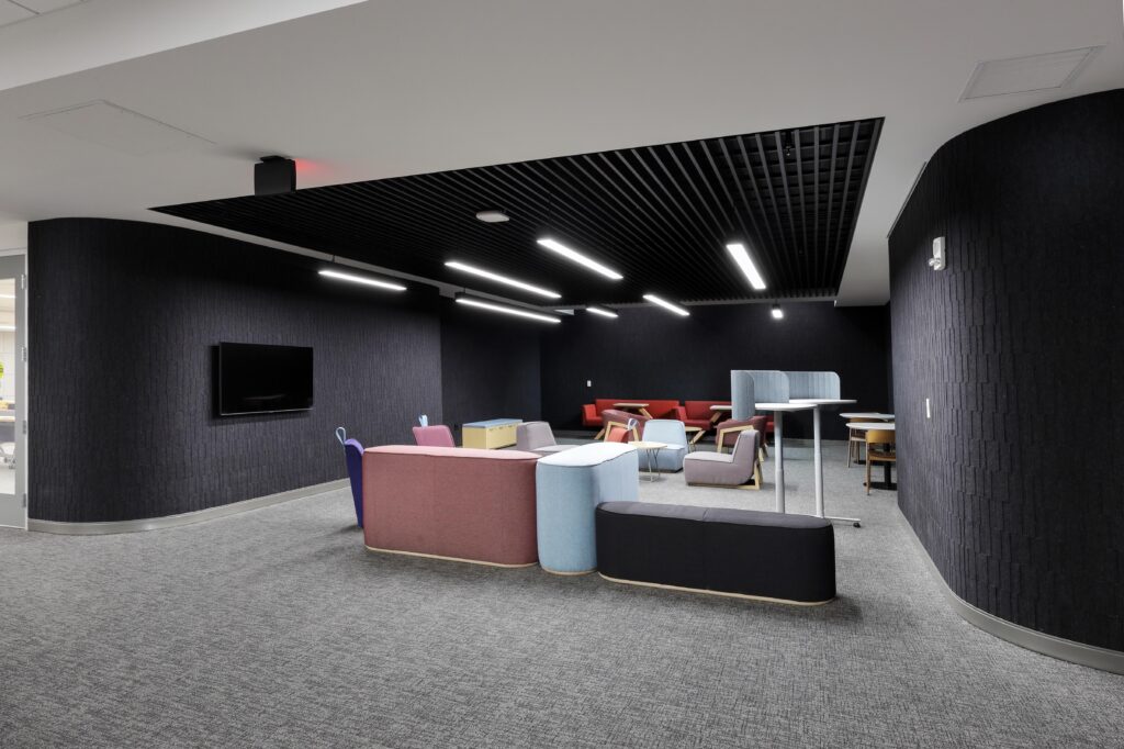 A modern lounge area with modular seating in shades of blue, pink, and grey arranged on a grey carpeted floor.