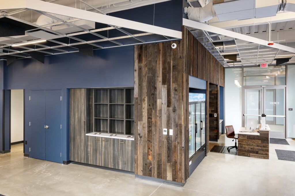 Office interior featuring a dark blue wall, wooden accent wall, storage cabinets, a glass-door refrigerator, and a reception desk with a chair.