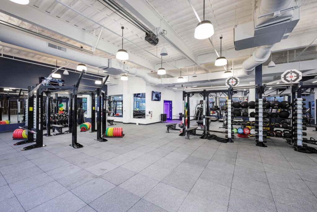 Spacious gym interior with weight racks, weight plates, and medicine balls arranged on the floor.