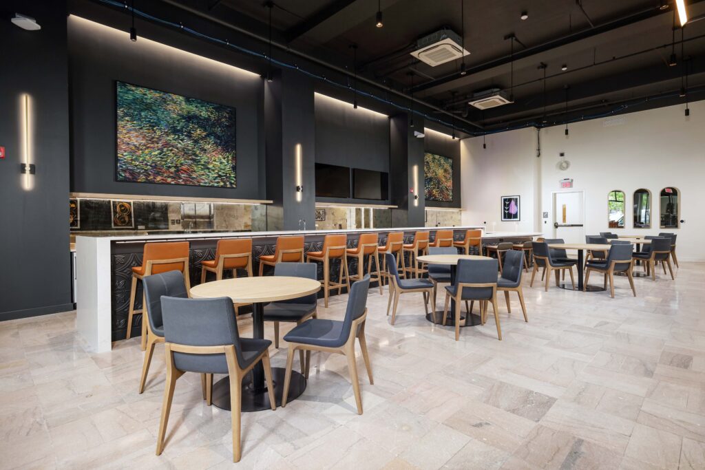 A restaurant interior featuring a bar with orange stools and a seating area with round tables and gray chairs.