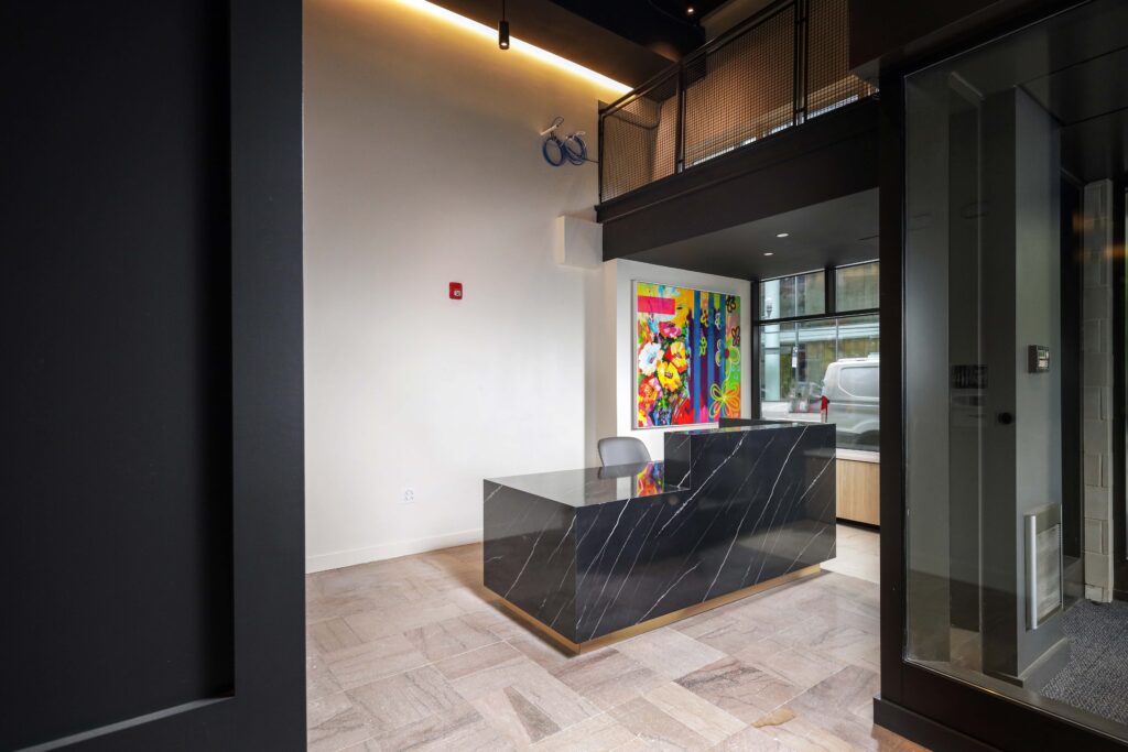 A black marble reception desk in a modern office lobby with a vibrant floral painting on the wall behind it.