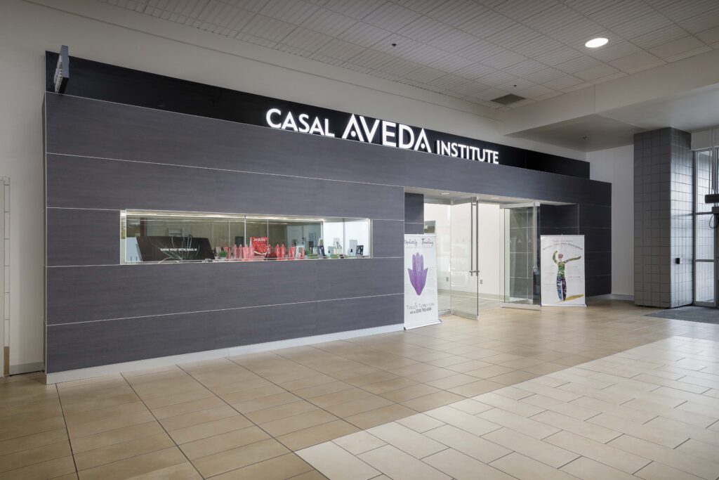 Exterior entrance of the Casal Aveda Institute storefront with display windows and two informational banners.
