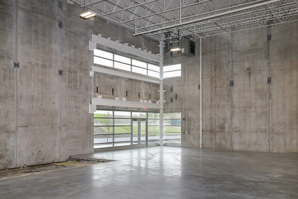 Empty warehouse space with concrete walls, high ceilings, and a glass storefront entrance.