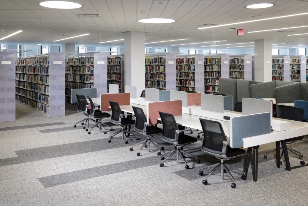 Rows of study desks with privacy dividers and rolling chairs in a library surrounded by tall bookshelves.