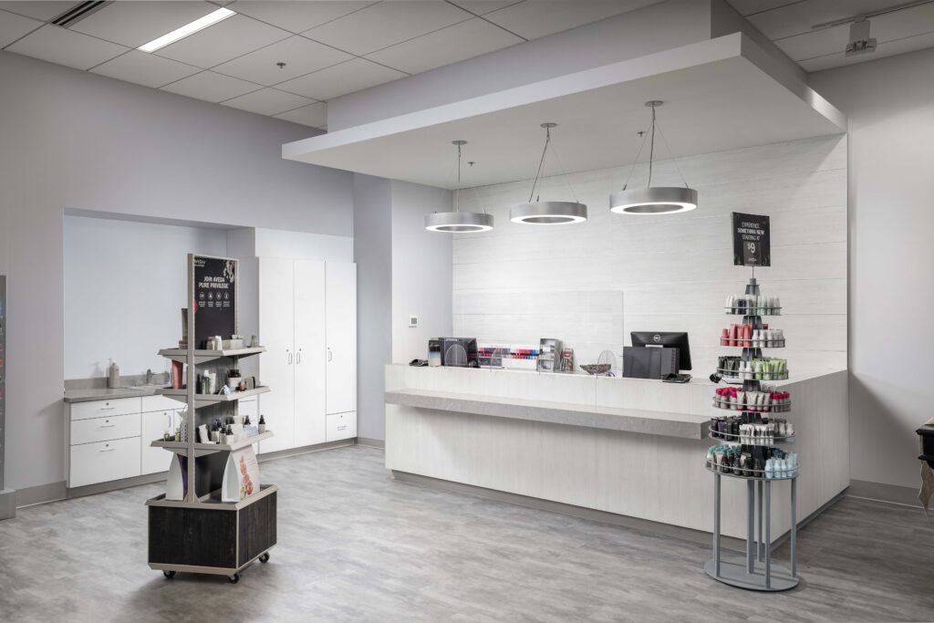 A salon reception area with a long service desk, a freestanding product display stand, and a tiered spinning rack of hair care products.