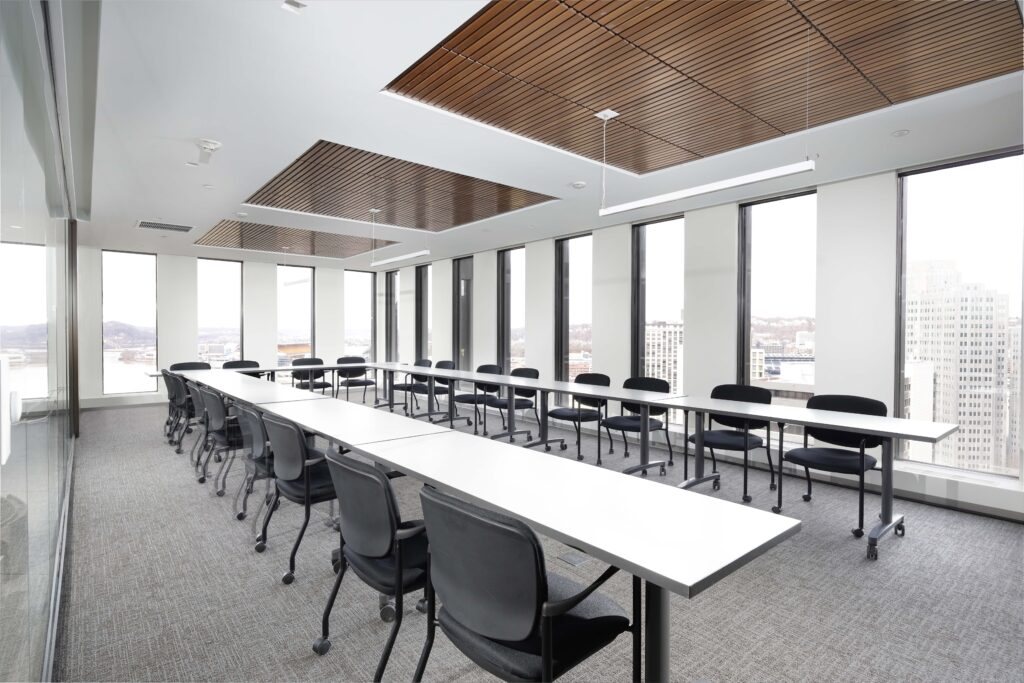 A bright conference room with white tables arranged in a U-shape and black rolling chairs.