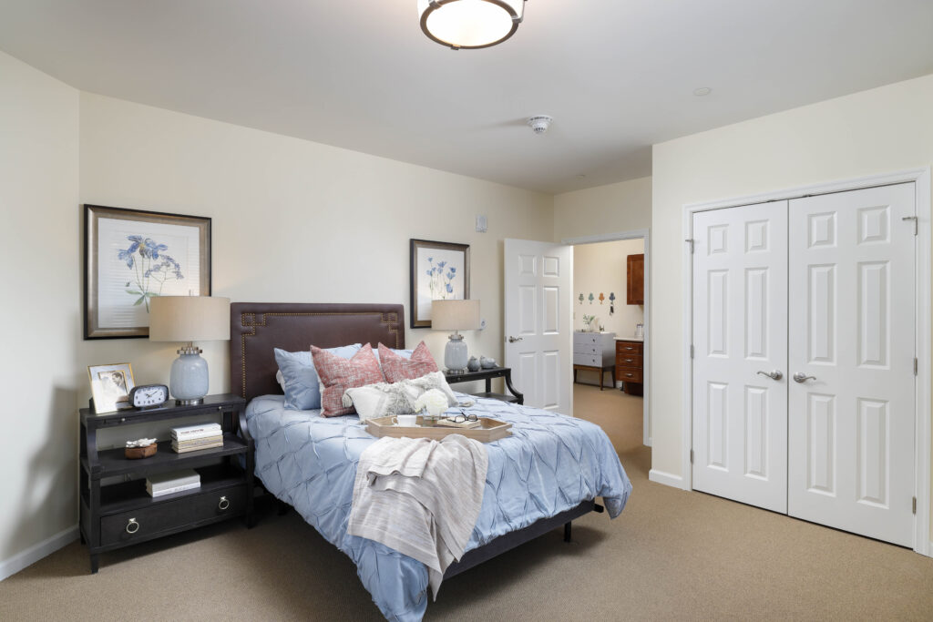 A bedroom with a queen-sized bed, blue bedding, and two dark wood nightstands, with an open doorway leading to a small hallway.