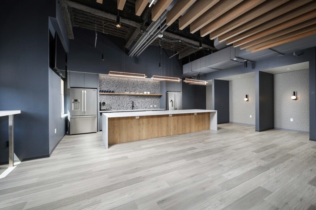 Modern office breakroom with a large kitchen island, stainless steel appliances, and a tiled backsplash.