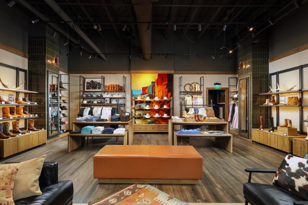 Interior of a western apparel store featuring shelves of cowboy boots, hats, and clothing with a central seating bench.