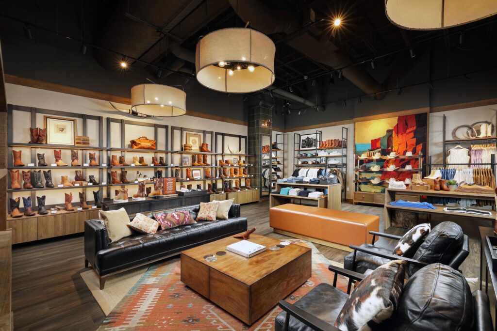 Interior of a western-style clothing store featuring shelves of cowboy boots, leather lounge furniture, and a patterned area rug.