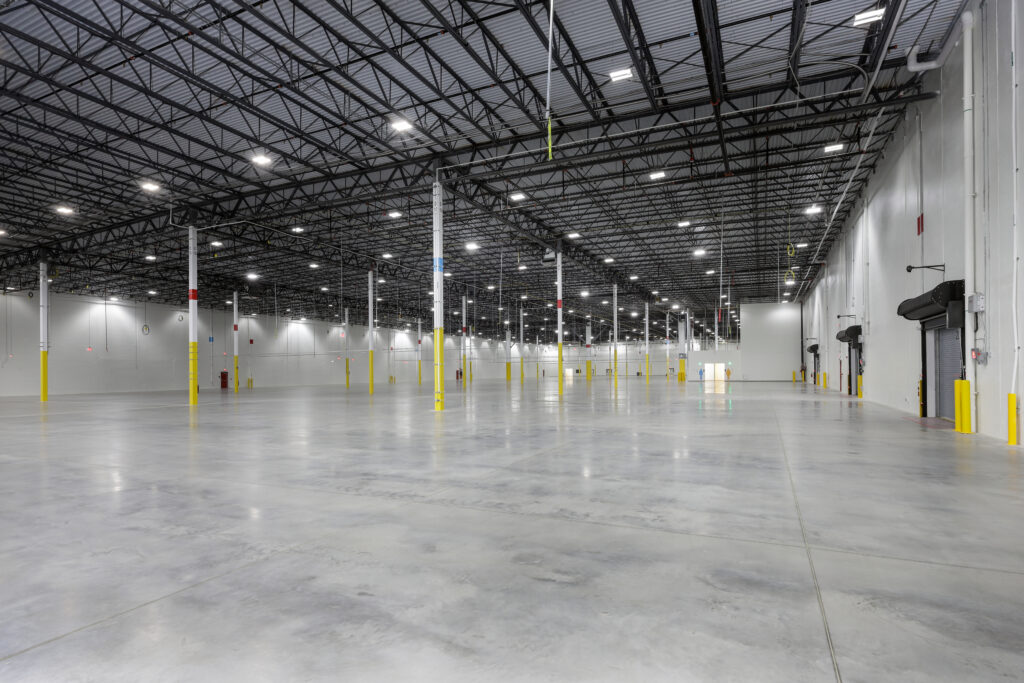 An expansive, empty warehouse with high ceilings, concrete floors, and evenly spaced support pillars marked with yellow paint.