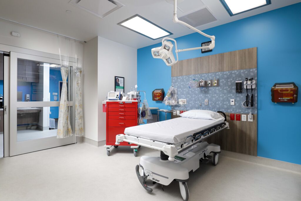 Hospital patient room with a gurney, a red medical cart, and a ceiling-mounted procedure light.