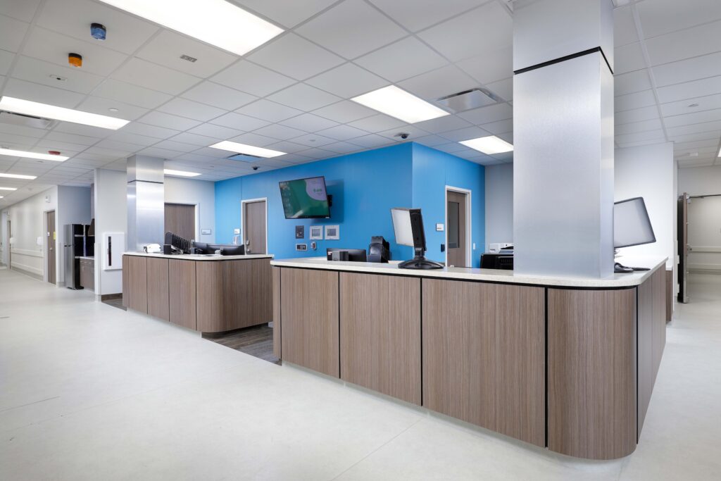 A reception desk with a wood-grain base and white countertop in a bright office with blue walls and a white drop ceiling.