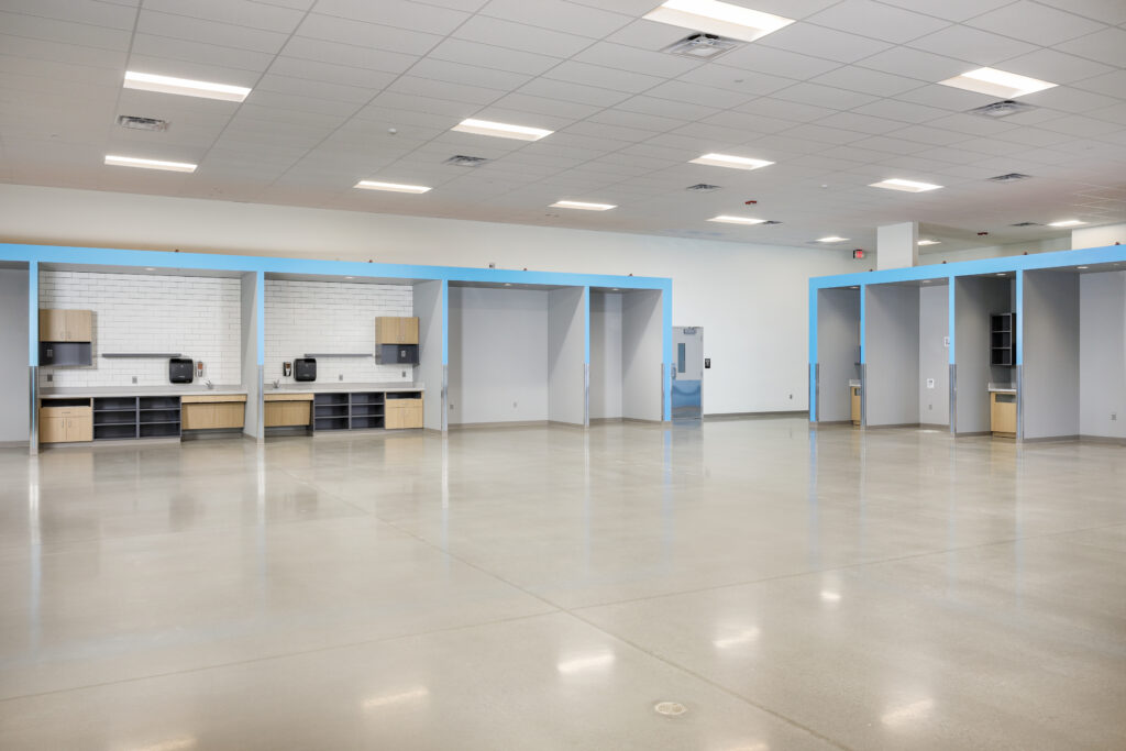 Large empty room with a polished concrete floor and multiple recessed alcoves featuring built-in cabinetry and white tiled backsplashes.