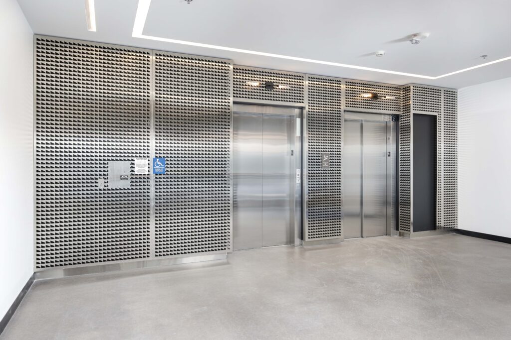 Two silver elevator doors set into a wall covered in a metallic, geometric patterned screen.