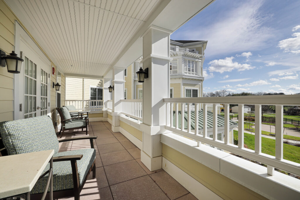 Covered balcony with cushioned armchairs overlooking a park.