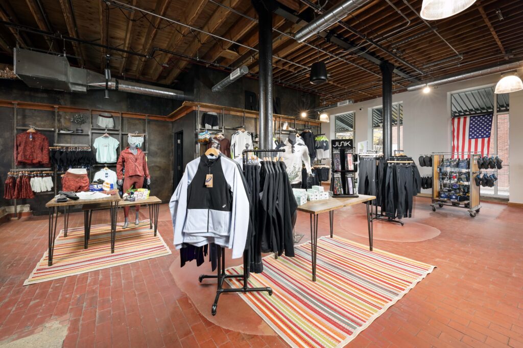 Interior of an athletic apparel store featuring clothing racks, mannequins, and tables displaying workout gear on striped rugs.