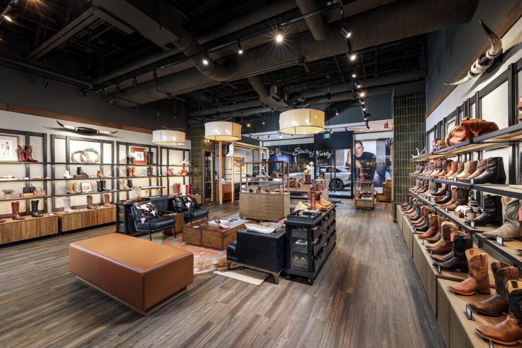 Interior of a western boot store featuring rows of footwear displayed on wall shelves, leather seating, and a large wooden coffee table.