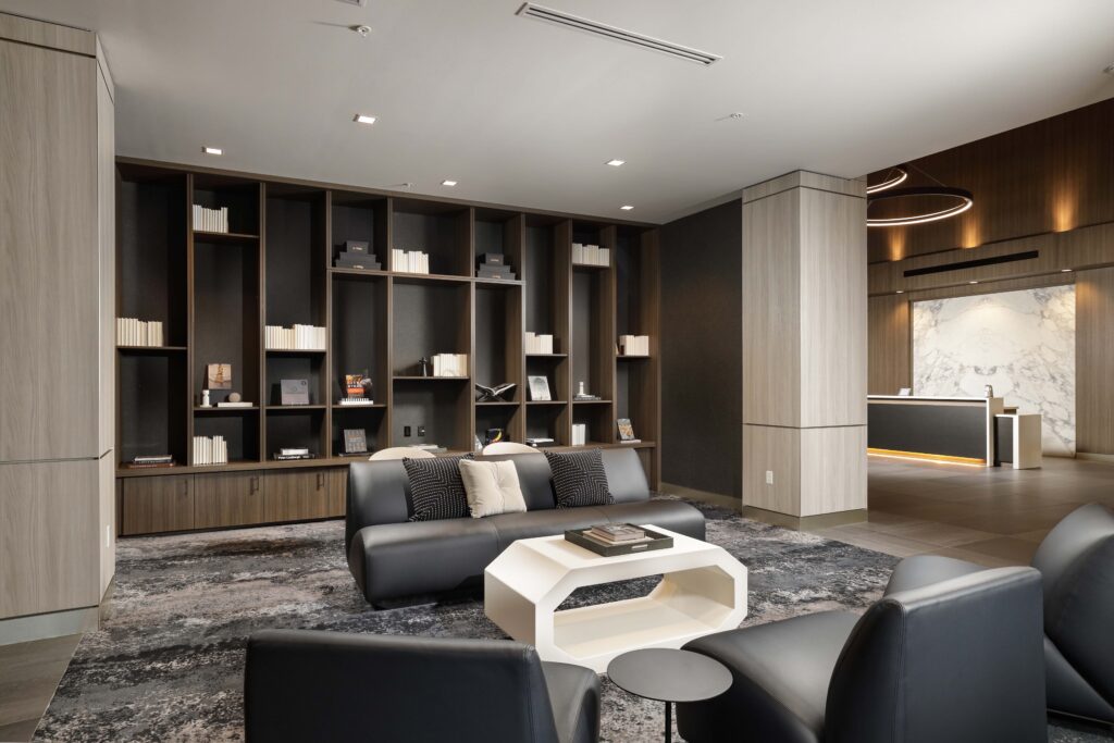 A modern lobby featuring a dark sofa, a geometric white coffee table, and floor-to-ceiling wooden bookshelves.
