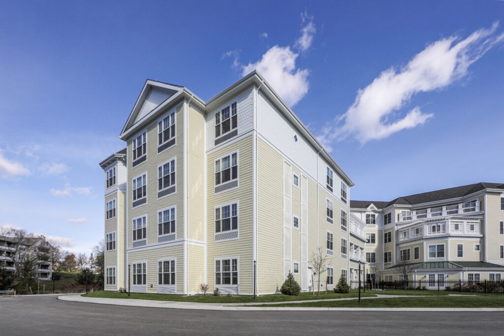 A multi-story apartment building with yellow siding and white trim under a blue sky.