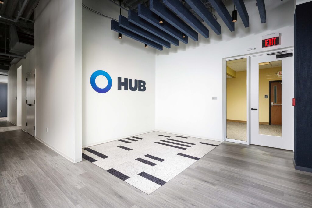 Office lobby with the Hub logo on the wall, a patterned area rug, and a doorway with an exit sign.