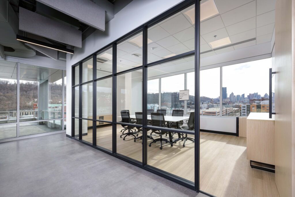 A glass-walled conference room with a table and chairs, overlooking a city skyline.