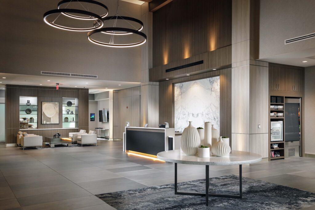 Hotel lobby featuring a reception desk, a central marble-topped table with white vases, and a lounge area with armchairs.