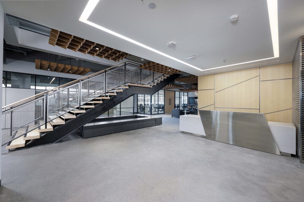 Modern office lobby with a metal and wood staircase, a angular reception desk, and concrete flooring.