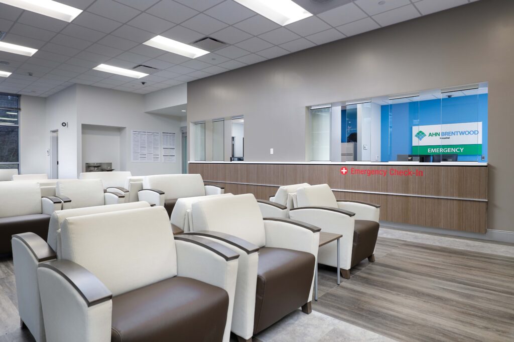Waiting area with rows of cream and brown chairs facing an AHN Brentwood Hospital emergency check-in desk.