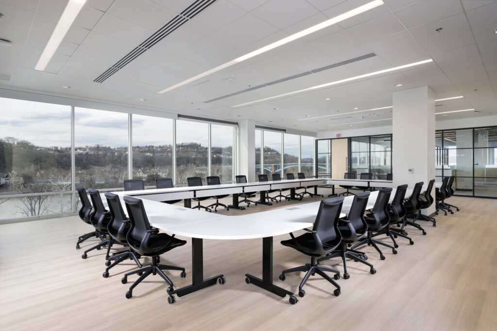 U-shaped conference table surrounded by black office chairs in a room with floor-to-ceiling windows overlooking a river and bridge.