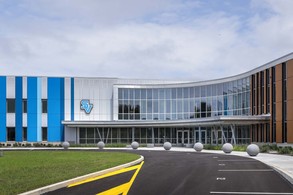 Exterior of a modern building with a curved glass facade and a blue logo featuring the letters SV.