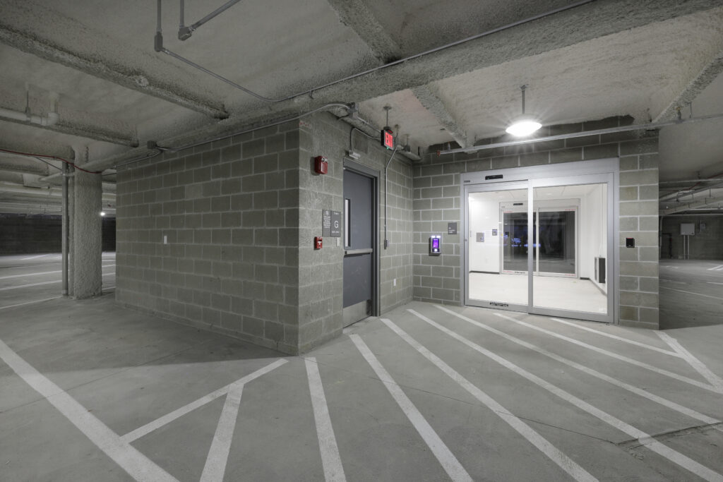 Concrete parking garage featuring an exit door and a sliding glass door entrance.