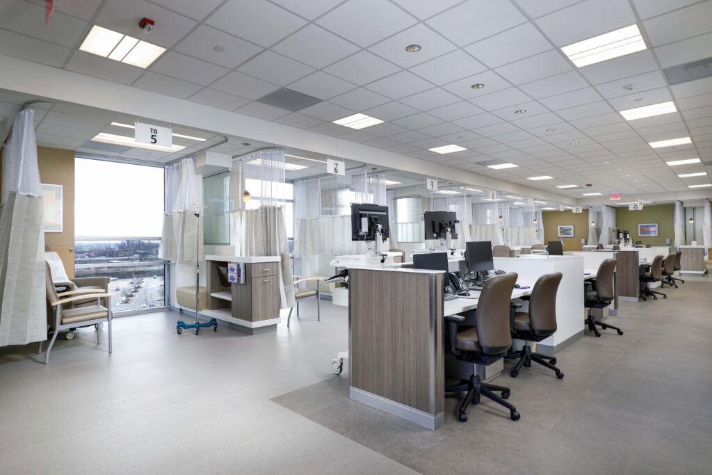 A modern medical infusion center featuring rows of computer workstations and partitioned treatment bays with chairs.