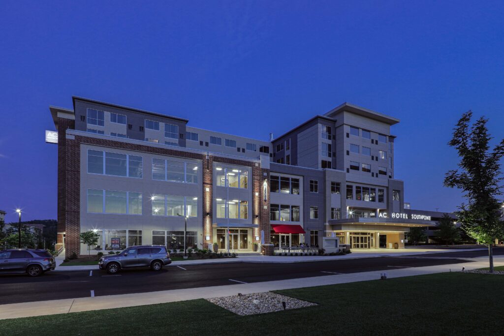 Exterior of the AC Hotel Southpointe at twilight, showing the building facade, parking lot, and entrance.